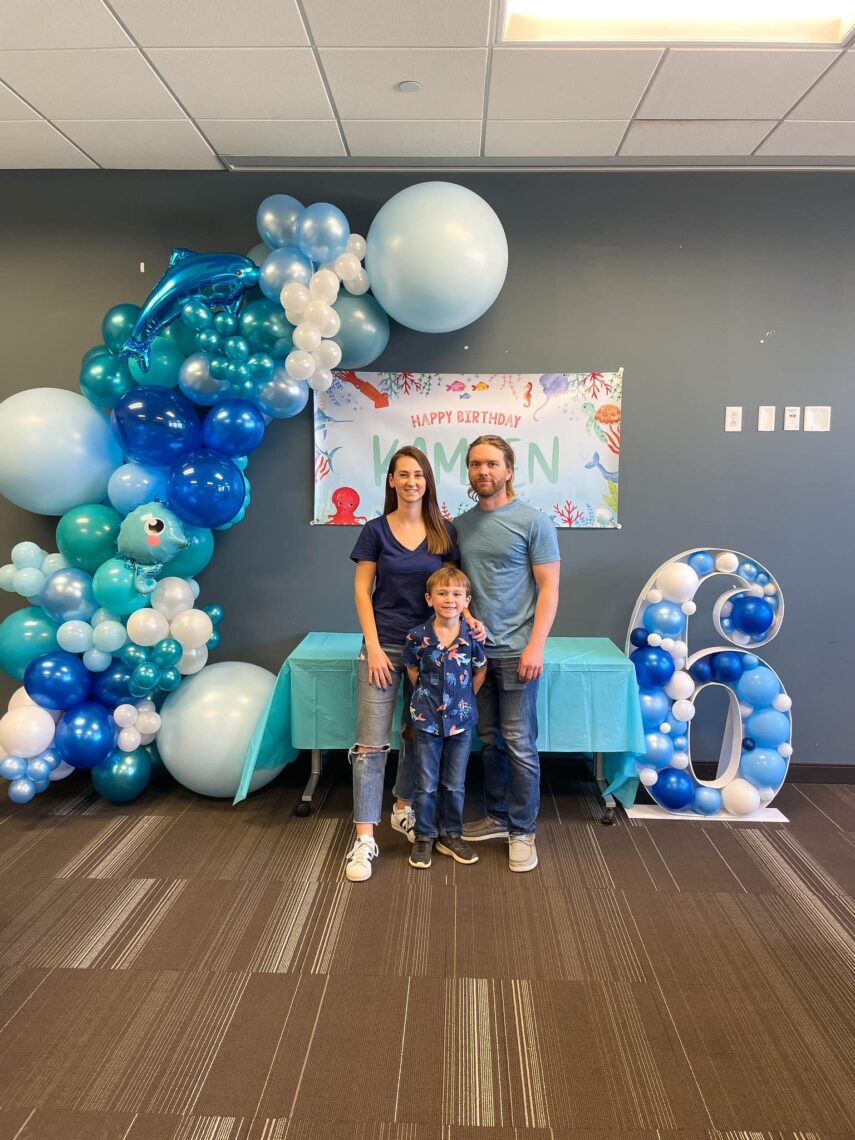 Family taking photo in front of balloon garland and birthday sign.